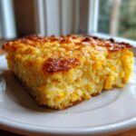 A close-up of a golden brown slice of moist corn casserole, rich with whole corn kernels.