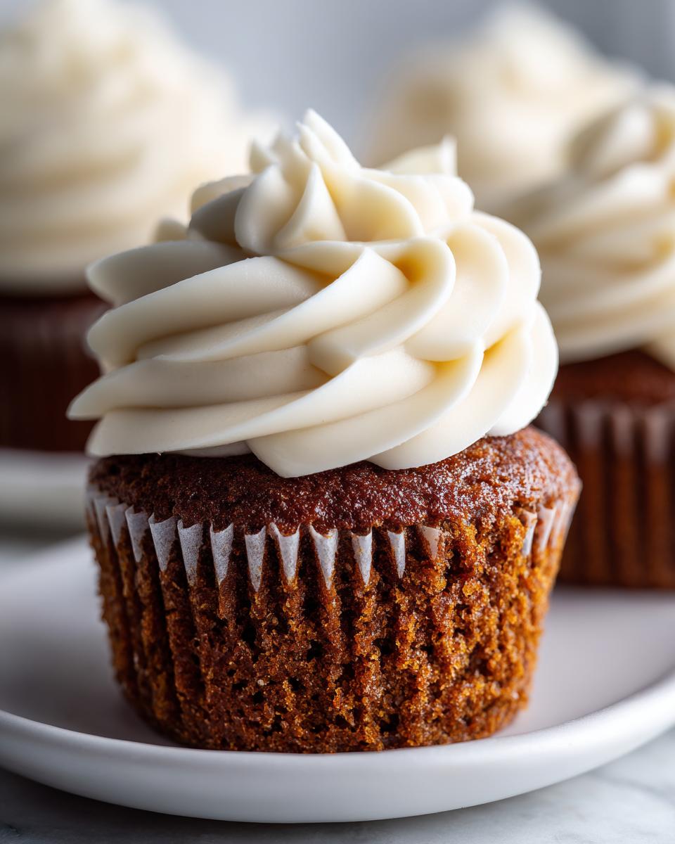 A close-up of one perfectly baked gingerbread cupcakes topped with a swirl of thick, creamy white frosting.