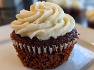 A close-up of a rich, dark brown gingerbread cupcake topped with a generous swirl of white cream cheese frosting.