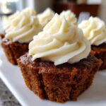 Close-up of rich, dark gingerbread cupcakes topped with swirls of creamy white frosting.
