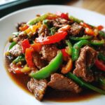 Close-up of savory pepper steak stir-fry featuring beef strips and bright green, red, and orange bell peppers in a rich sauce.