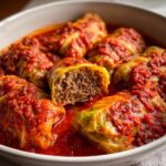 Close-up of juicy Stuffed Cabbage Rolls simmered in a rich, vibrant red tomato sauce, one roll cut open showing the meat filling.