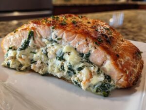 Close-up of a perfectly cooked piece of stuffed salmon, showing the creamy spinach and seafood filling spilling out.