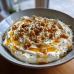 A bowl of creamy whipped ricotta dip drizzled with honey and topped with chopped walnuts and herbs.