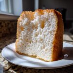 A tall, fluffy slice of angel food cake showing its airy white interior and golden crust.