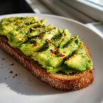 Close-up of delicious avocado toast, sliced avocado topped with chili flakes and sesame seeds on toast.