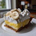 A close-up of a slice of banana cream pie showing creamy custard, graham cracker crust, and fresh banana slices.