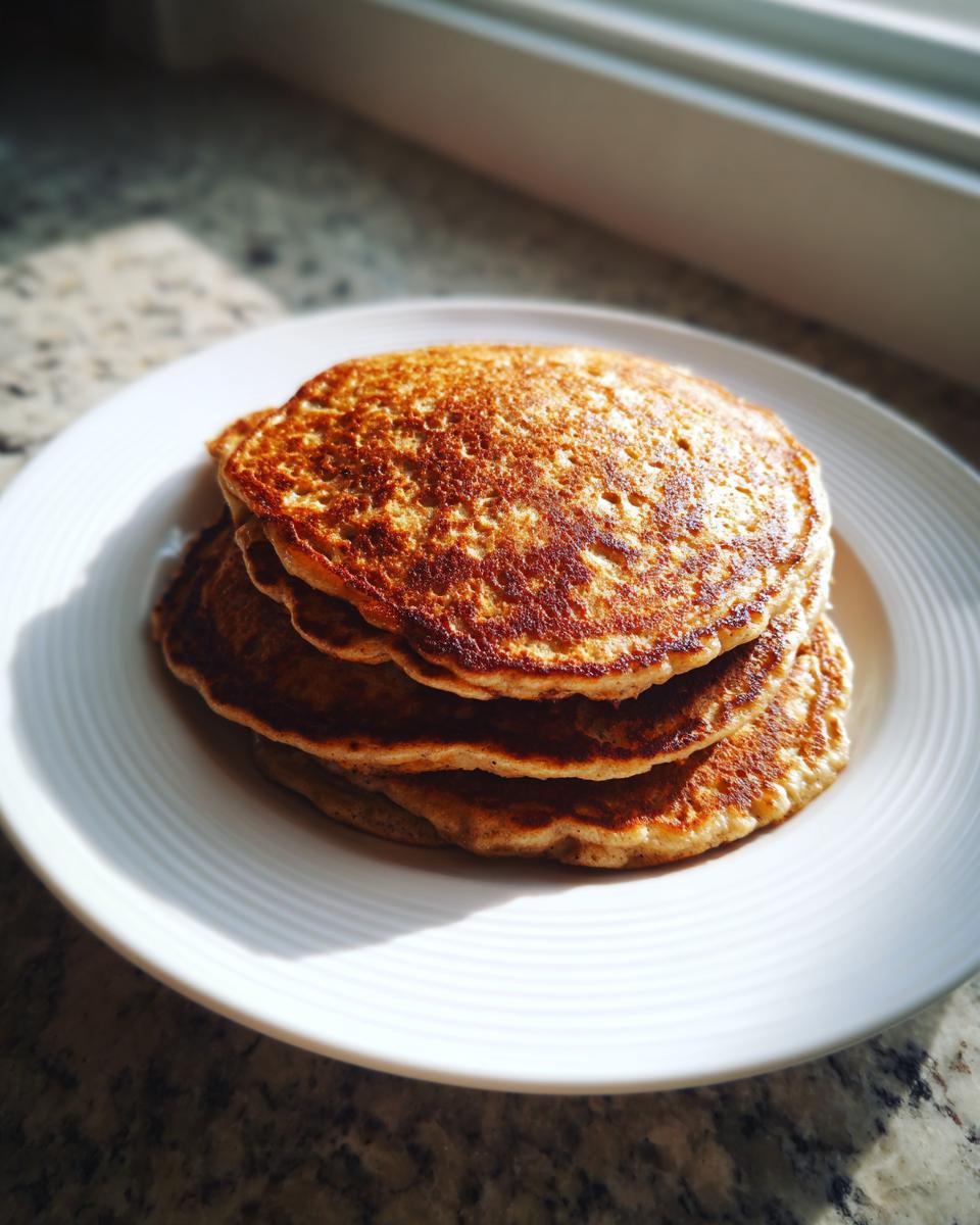 A stack of three golden-brown banana oatmeal pancakes served on a white plate near a window.