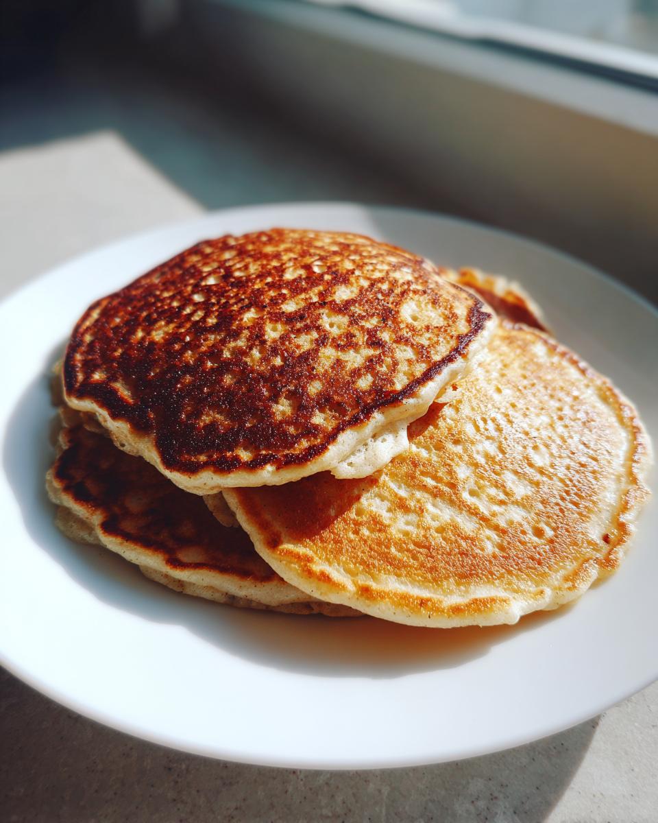 A stack of three golden brown banana oatmeal pancakes served on a white plate, lit by sunlight.