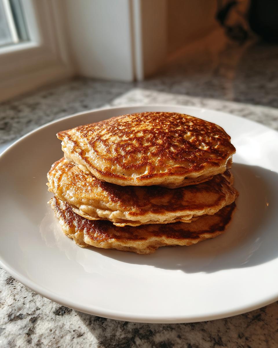 A stack of three golden brown banana oatmeal pancakes on a white plate, lit by sunlight.