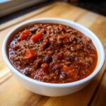 Close-up of a white bowl filled with rich, thick chili featuring ground meat, kidney beans, and chunks of tomato, showcasing the best chili recipe.