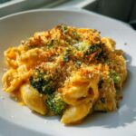A serving of creamy broccoli cheddar casserole topped with golden, crunchy breadcrumbs and fresh herbs.