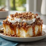A moist slice of butter pecan praline poke cake topped with whipped cream and chopped pecans.