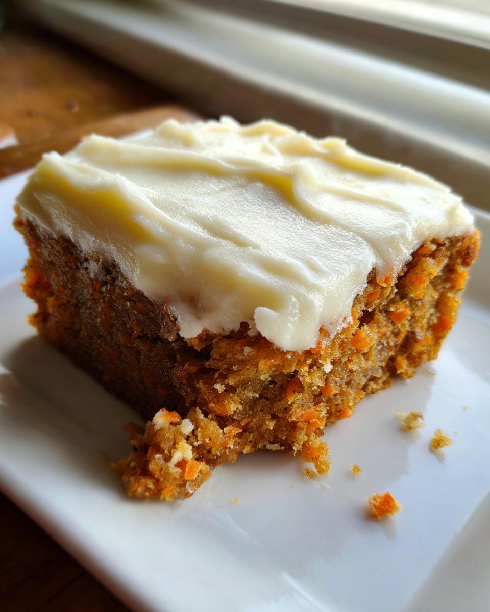 A single square of moist carrot cake bars topped with thick cream cheese frosting, served on a white plate.