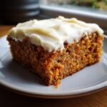 A thick, square slice of moist carrot cake bars topped with generous cream cheese frosting.