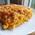 A close-up of a serving of creamy, cheesy baked mac and cheese recipe with a golden breadcrumb topping.