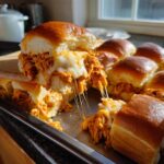 A close-up of one of the buffalo chicken sliders being lifted, showing melted, stringy cheese stretching between the halves.