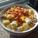 A close-up of a creamy bowl of chicken corn chowder topped with bacon bits and shredded cheese.