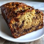 A close-up view of a freshly baked loaf of chocolate chip banana bread recipe, sliced on a white plate.