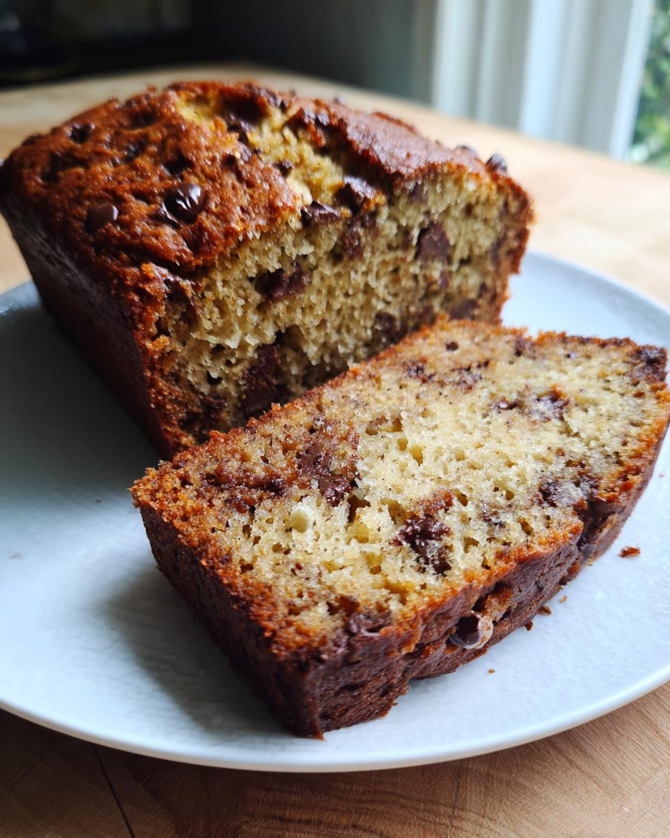 A moist slice cut from a loaf of chocolate chip banana bread recipe, showing rich texture and melted chips.