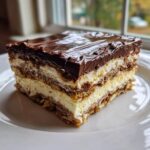 A perfectly layered slice of chocolate eclair cake featuring graham crackers, vanilla cream, and rich chocolate frosting.