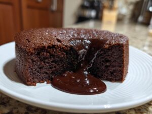 A close-up of a freshly baked chocolate pudding cake with a section cut out, revealing rich, molten chocolate sauce flowing onto a white plate.