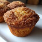 A close-up of a golden brown cinnamon sugar french toast muffins, heavily coated in sparkling cinnamon sugar.