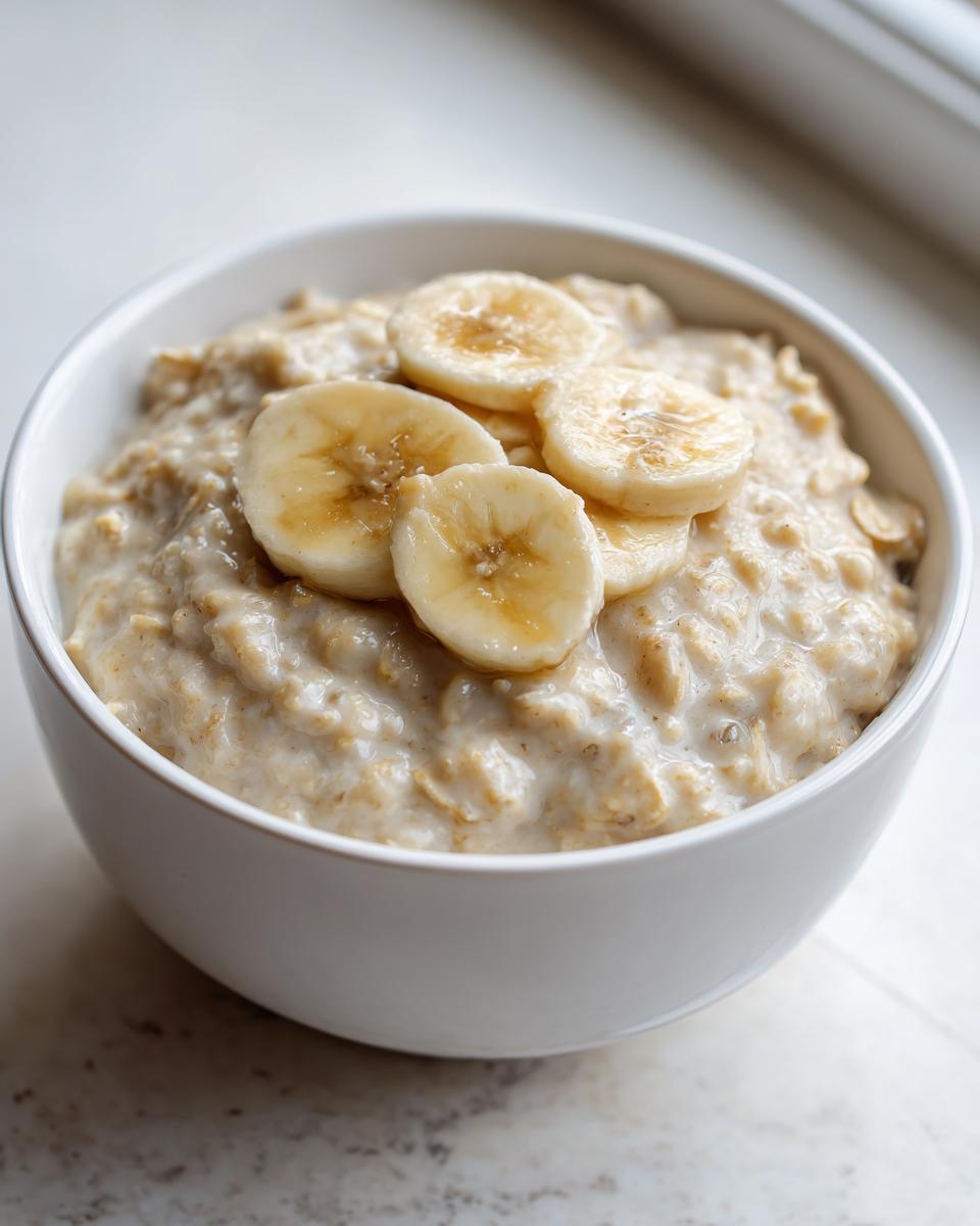 Close-up of creamy banana oatmeal in a white bowl, topped with fresh banana slices.