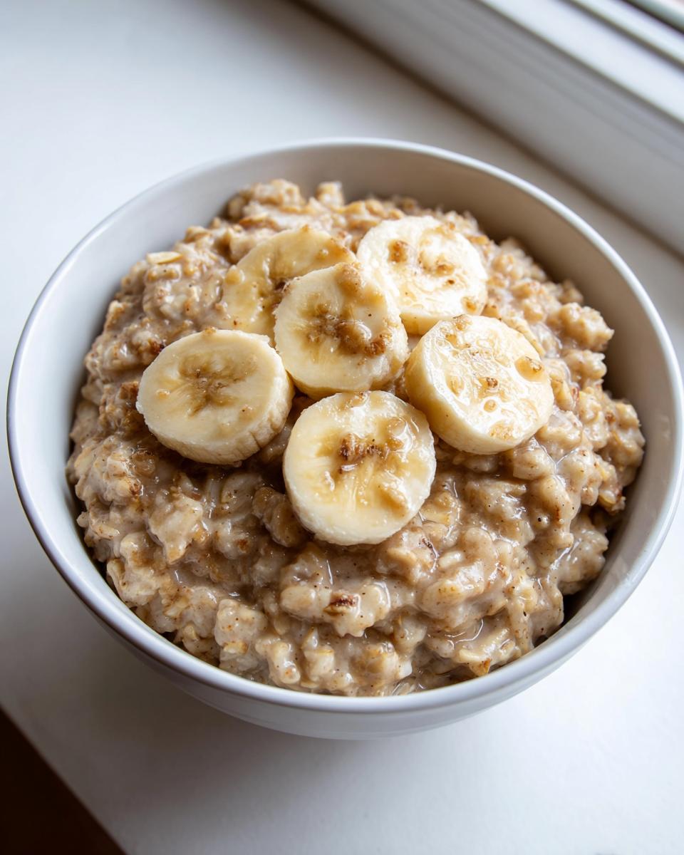 A close-up of creamy banana oatmeal in a white bowl, topped with five slices of fresh banana.