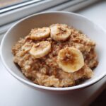 Close-up of creamy banana oatmeal topped with sliced bananas, cinnamon, and a drizzle of syrup.