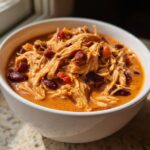 Close-up of creamy buffalo chicken chili featuring shredded chicken and dark red kidney beans in a white bowl.