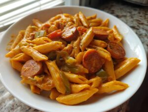Close-up of a white bowl filled with creamy Cajun sausage pasta featuring penne, sliced smoked sausage, and green peppers.