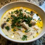 Close-up of a bowl of creamy chicken coconut soup topped generously with fresh cilantro and sliced mushrooms.