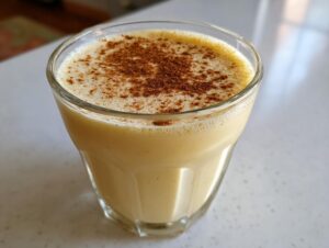 Close-up of a glass of creamy, pale yellow eggnog topped with a dusting of cinnamon.
