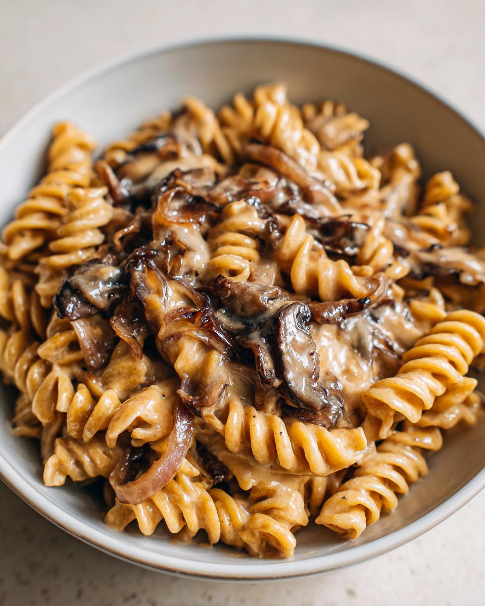 Close-up of creamy french onion pasta made with fusilli, topped with caramelized onions and mushrooms.