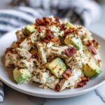 A close-up of creamy honey mustard chicken salad topped with crispy bacon bits and fresh avocado chunks.