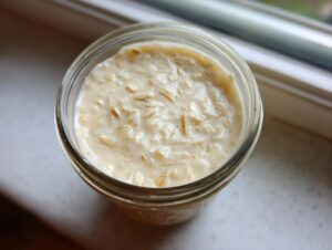 Overhead close-up of creamy overnight oats soaking in milk inside a clear glass jar.