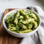 A white bowl filled with penne pasta coated in rich, creamy pesto pasta sauce.