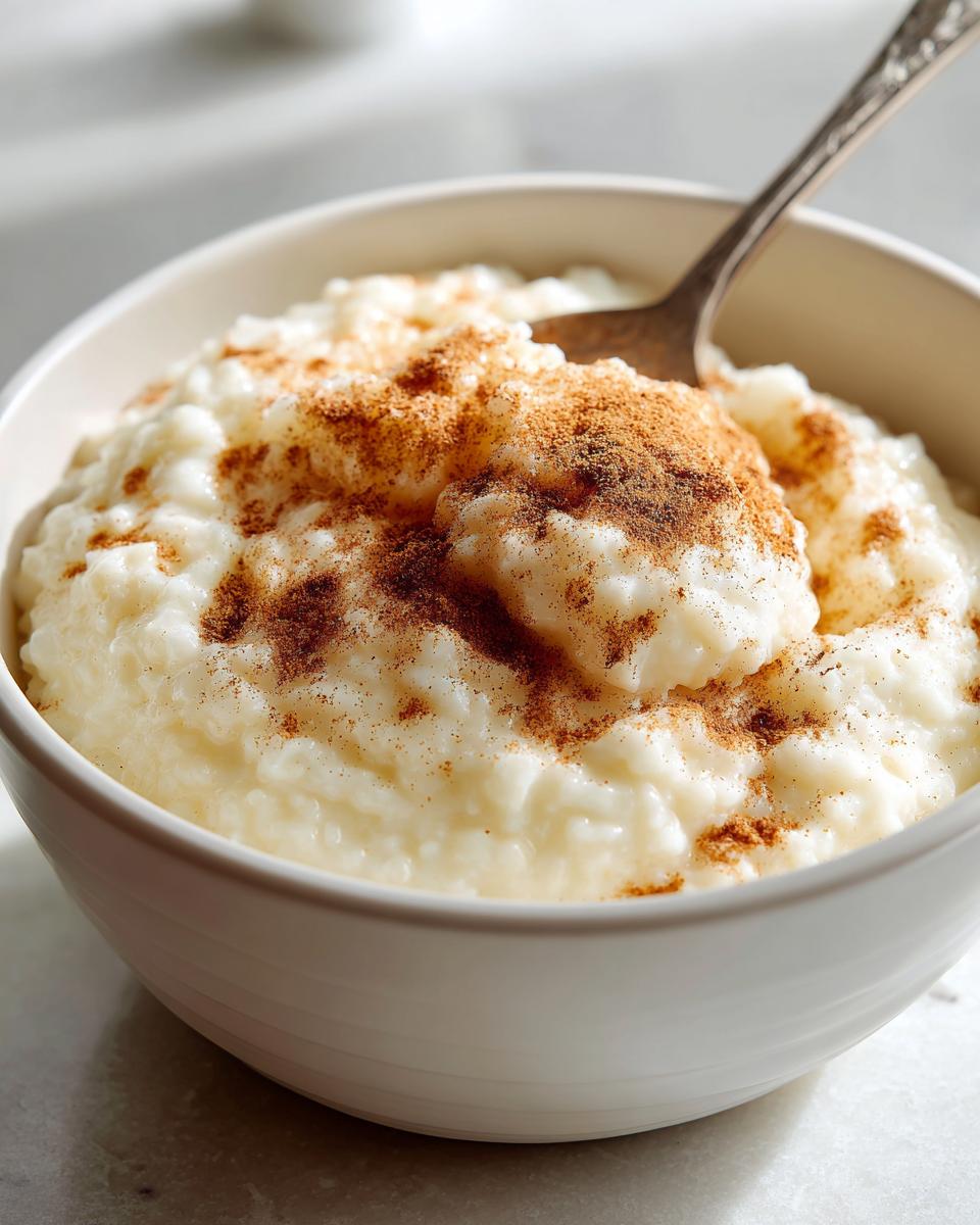 Close-up of creamy rice pudding in a white bowl, generously topped with ground cinnamon.