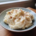 A close-up of creamy roasted garlic mashed potatoes topped with crispy browned bits, served in a light blue bowl.