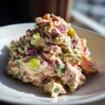 A mound of creamy salmon salad mixed with chopped red onion and celery, served on a white plate.