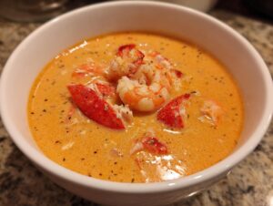 Close-up of a creamy, orange-hued seafood soup topped with bright red lobster pieces and plump shrimp.