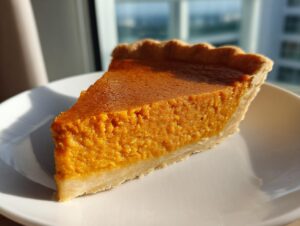 A close-up shot of a thick slice of easy pumpkin pie resting on a white plate, bathed in sunlight.
