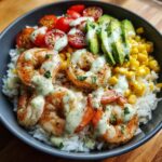 Close-up of a delicious shrimp bowl featuring grilled shrimp over rice, topped with avocado, corn, tomatoes, and a creamy green sauce.