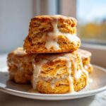 A stack of three fluffy sweet potato biscuits drizzled generously with a thick vanilla glaze.