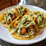 Four fully loaded shrimp taco shells filled with cabbage slaw, seasoned shrimp, and drizzled with a bright green creamy sauce.