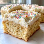 A thick slice of soft sugar cookie bars topped with white frosting and colorful rainbow sprinkles.