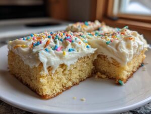 Two squares of thick, moist sugar cookie bars topped with creamy white frosting and colorful rainbow sprinkles.