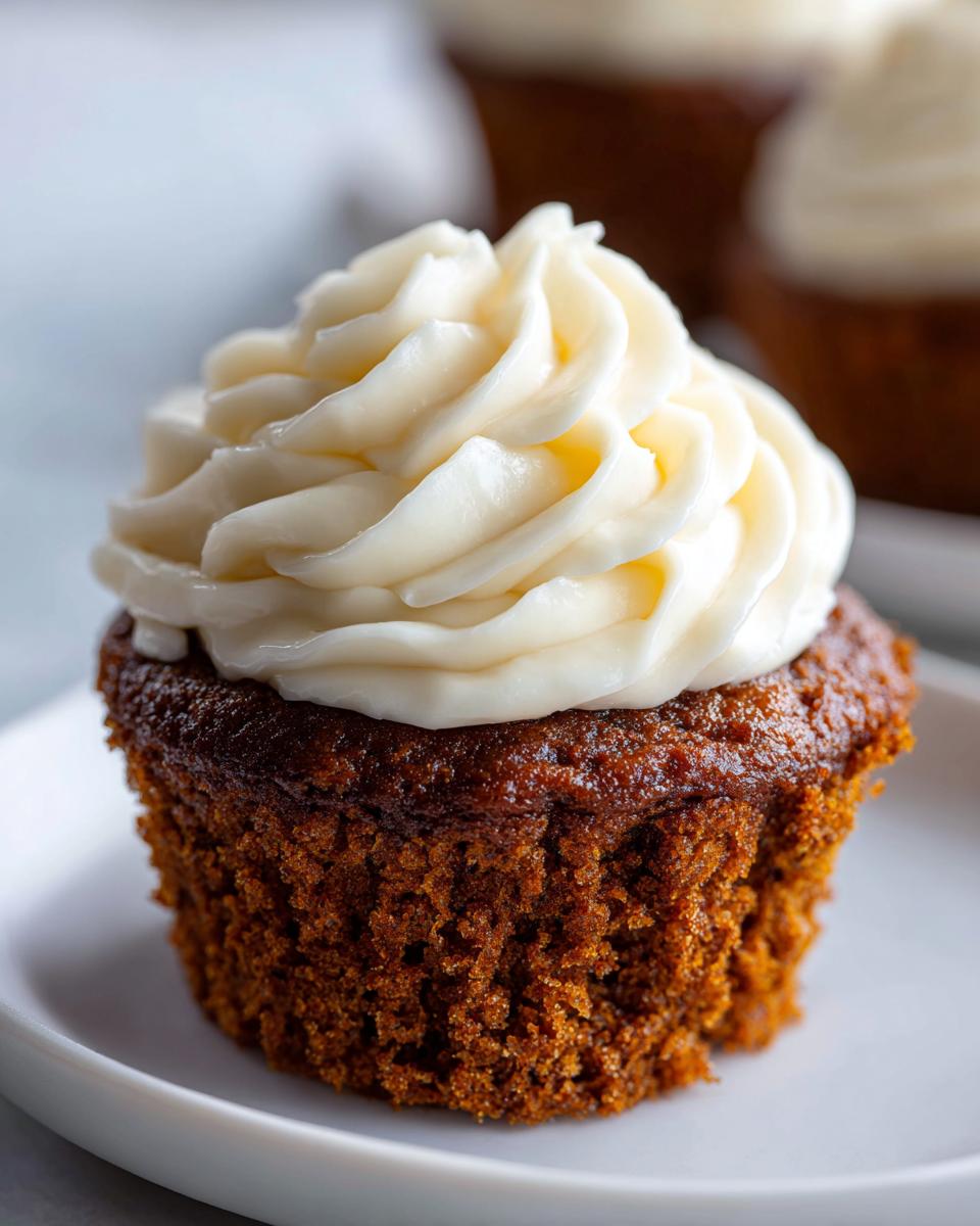 A close-up of a rich, dark gingerbread cupcakes topped with a swirl of thick, creamy white frosting.