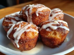 A stack of golden-brown, freshly baked cinnamon roll bites drizzled generously with white icing.